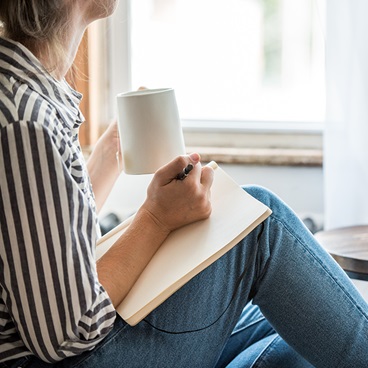 Woman writing & drinking from a mug.