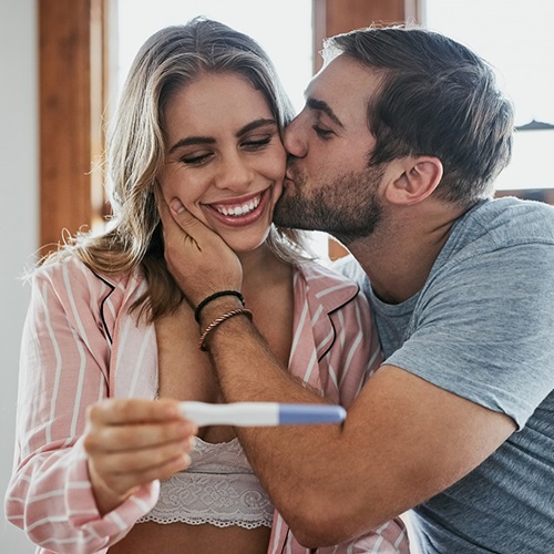 Man kissing woman, whilst woman smiles at pregnancy test