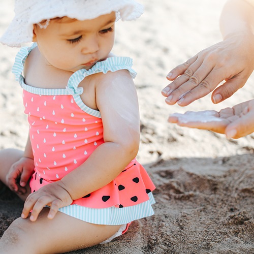 Mother applying sunscreen on her newborn at the beach.
