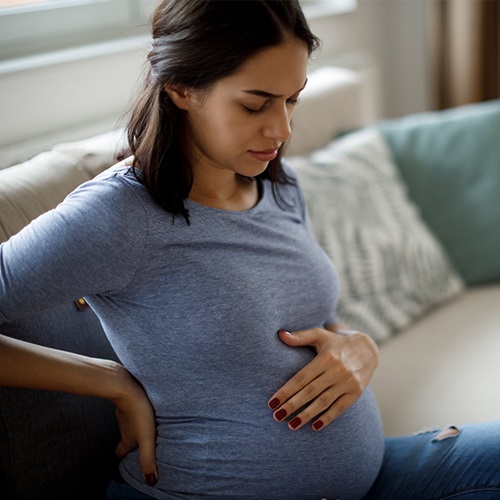 Pregnant mother holding her back & baby bump in discomfort.