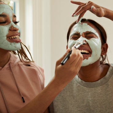 Young women laughing while putting on a face mask